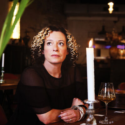 Kate Rusby sits at a table looking to the distance, with a glass of wine and lit candle 