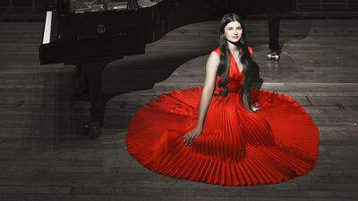 A young girl wearing a red dress sitting on the floor next to a grand piano