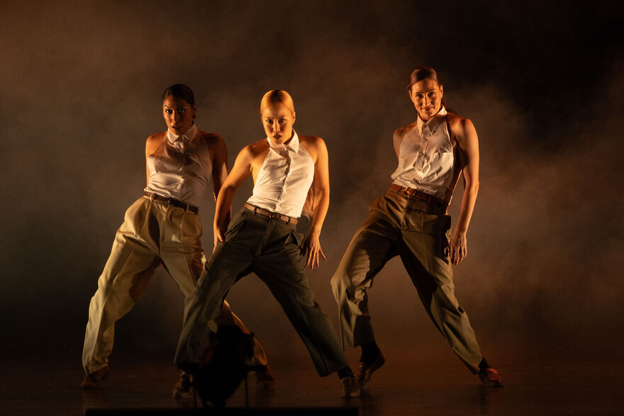 The 3 female dancers in Femme Fatale in a triangle formation. They are wearing formal clothes.