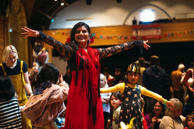 A lady in traditional dress dances in the middle of an audience. Her arms are reaching out in welcome.