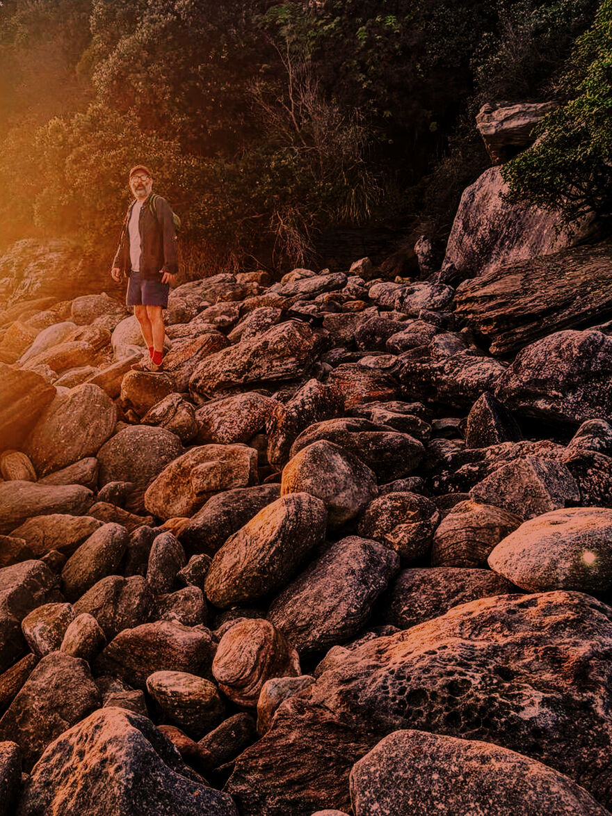 Daniel Kitson standing on a mound of rocks at dusk