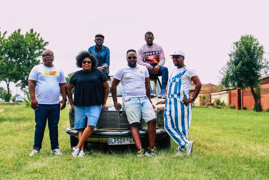 A group of people from South Africa stand around a car that is parked on grass