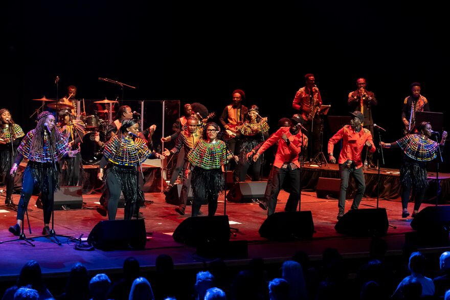 several members of the London African Gospel Choir on stage wearing traditional african clothing and the band playing in the background