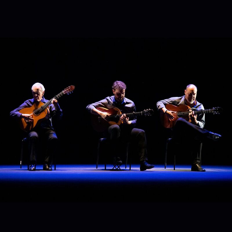 Three flamenco guitarists under dim lighting