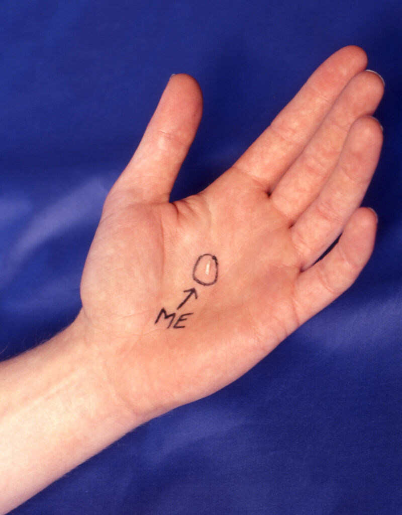 A close up of a hand, palm up. Written on the palm is the word 'me' with an arrow pointing to a circled grain of rice.
