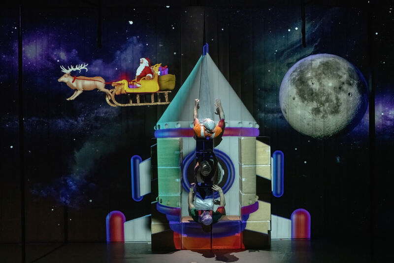 A projection shows a rocket with performers climbing out of it and santa and the sleigh in the background