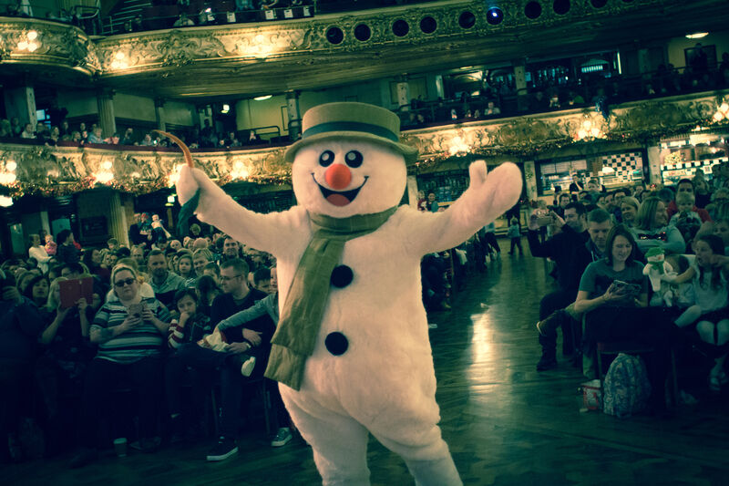 Snowman mascot walking through a concert hall with their hands up