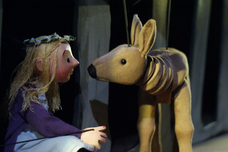 A wooden little girl puppet stares into the eyes of a wooden deer puppet