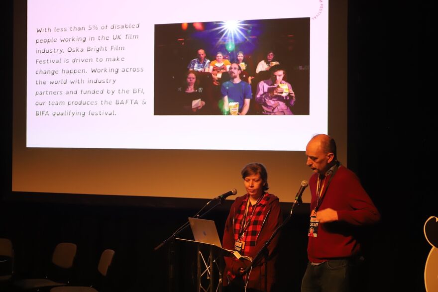 Two people are stood in front of a screen presenting