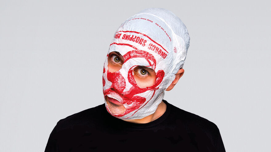 A man wearing a black t-shirt and a mask made from a white plastic shopping bag