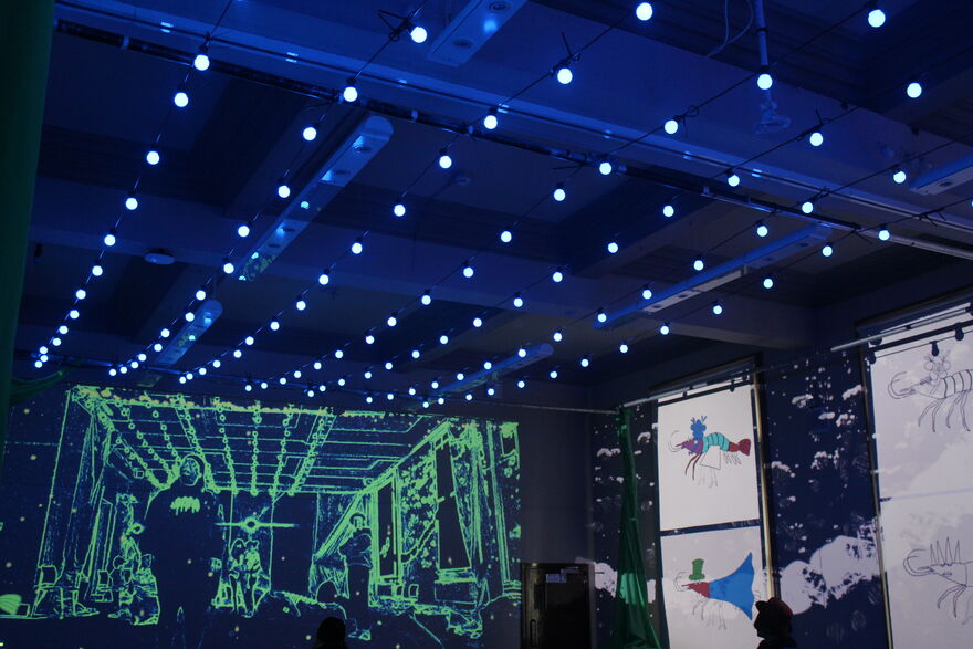 A dark room with rows of lights along the ceiling and colourful projections on the walls