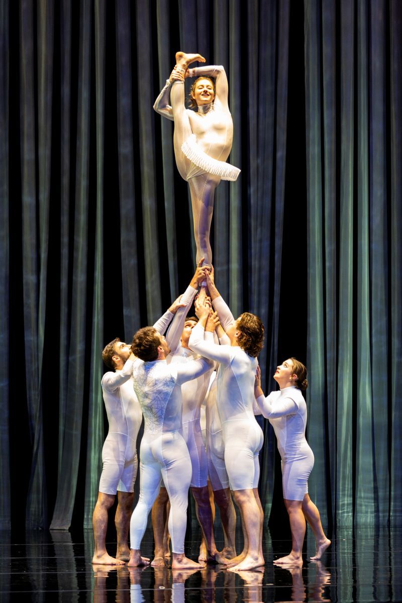 Lots of people are holding up on person by one leg. Their other leg is being held up to their head