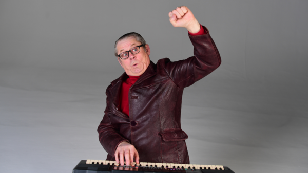 John Shuttleworth playing a small electric keyboard with a fist in the air