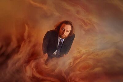 Rob Auton staring up wearing a blazer and blue tie. He is surrounded by red smoke and haze