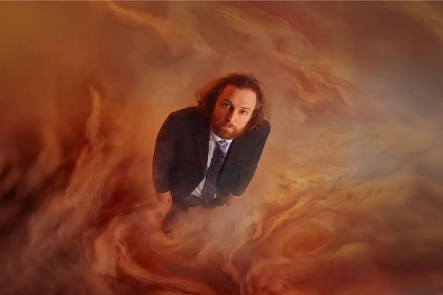 Rob Auton staring up wearing a blazer and blue tie. He is surrounded by red smoke and haze
