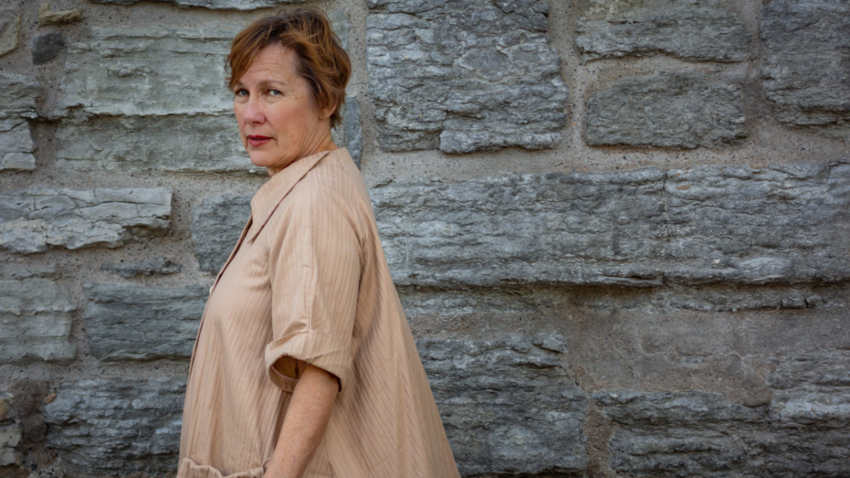 Iris DeMent against a brick wall looking into camera