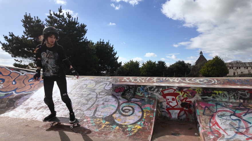 A person on a skateboard and wearing a helmet traverses a skate park. There is lots of graffiti on the skatepark