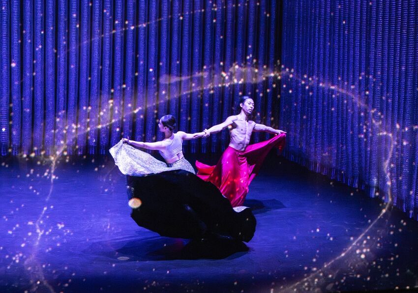 Two dancers twirling in floaty costumes, with glittering light projections around them
