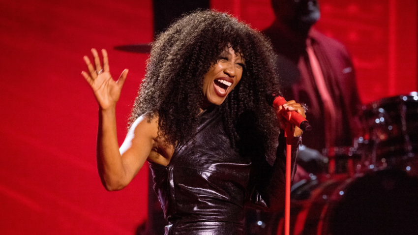 Woman sings into red microphone on a stage