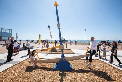 A large seesaw on some pebbles on Brighton Seafront, in the background is the West Pier
