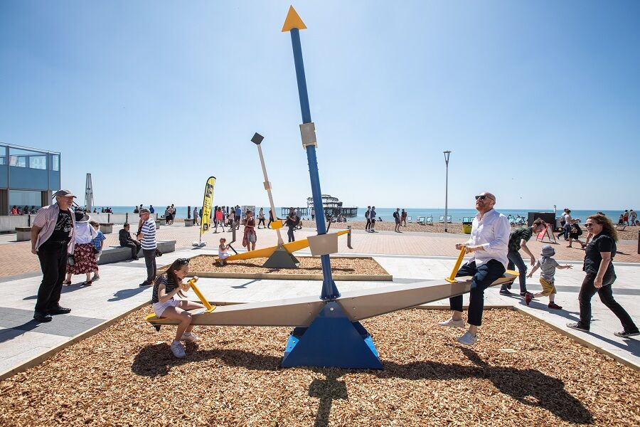 A large seesaw on some pebbles on Brighton Seafront, in the background is the West Pier