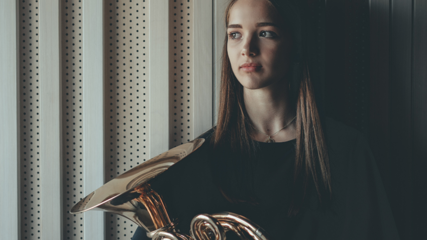 Woman wearing dark clothing holds a musical horn in her hand and looks into the distance