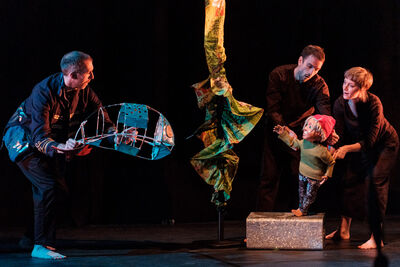 A puppet of a young boy and a puppet fish interact with fabric seaweed hanging from above 