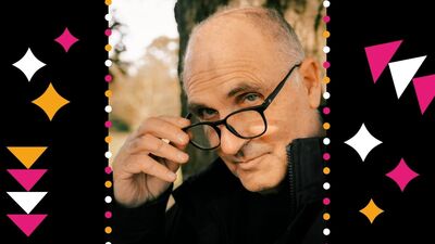 John Crace holding his glasses down with one hand and looking at the camera. He is surrounded by black, pink and white stars and triangles