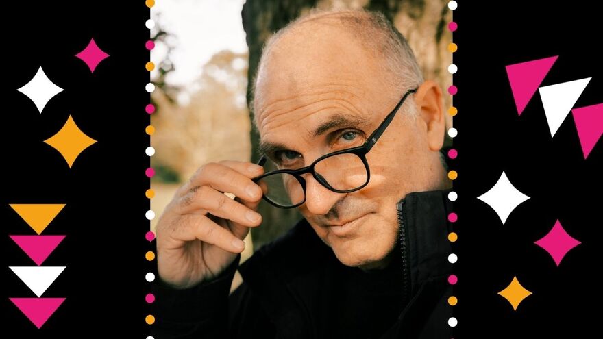John Crace holding his glasses down with one hand and looking at the camera. He is surrounded by black, pink and white stars and triangles