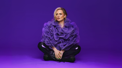 Joanne McNally against a purple backdrop in a purple big coat