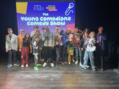 Sixteen young comedians pose for a photo with Comedian Michael Akadiri infront of a projected screen with 'The Young Comedians Comedy Show'