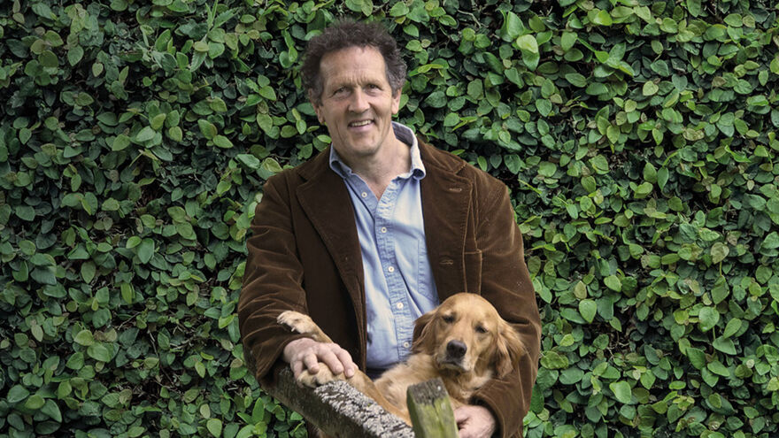 Monty Don standing in front of a green bush, with a dog 