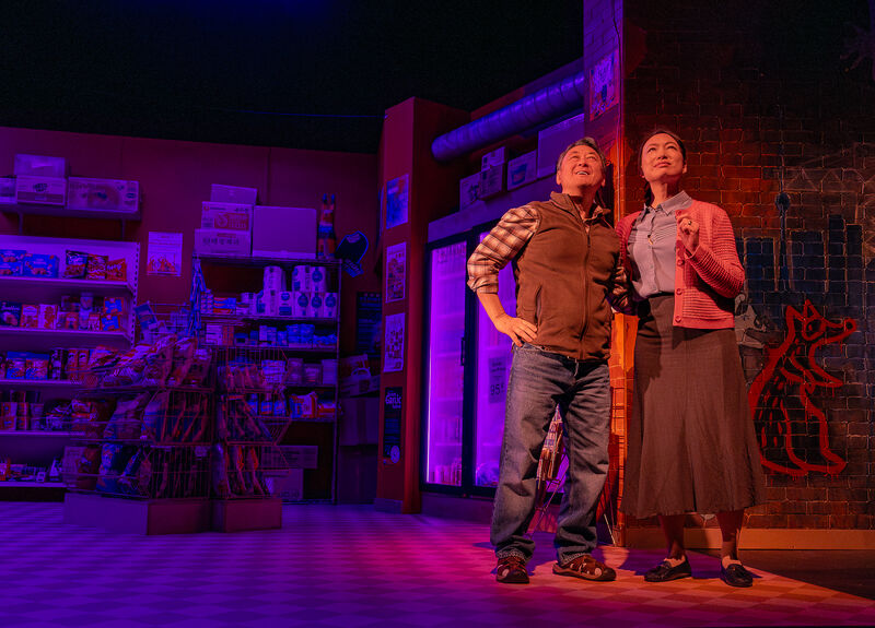 Two actors standing on a stage lit by dramatic blue and red lighting