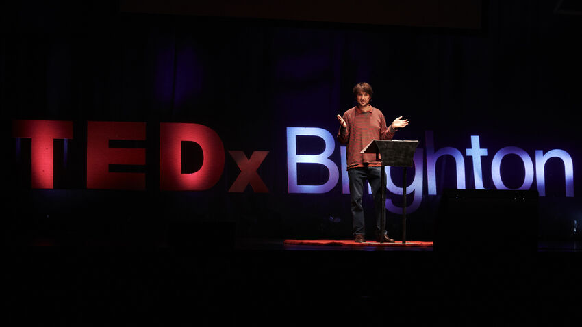A speaker performing on Brighton Dome's stage in front of a large, illuminated 'TEDx Brighton' sign