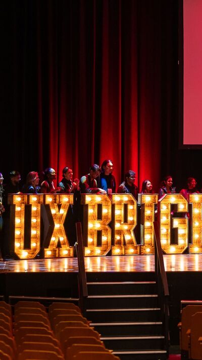 UX Brighton in light letters on stage with people standing behind