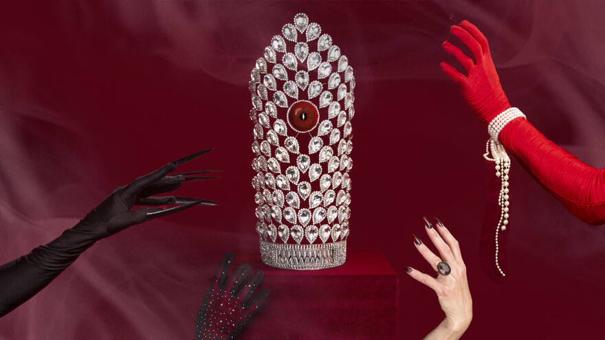 A diamond crown on a red velvet box. Four arms are reaching out towards the crown. Some are wearing gloves and jewelry
