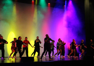 Dancers on stage in front of multi-coloured lights 