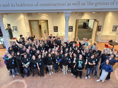 A group of volunteers stand in the Brighton Dome Foyer. They are all cheering and smiling at the camera