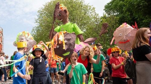 A group of children parade through the street with giant sculptures. They are all smiling and having a good time