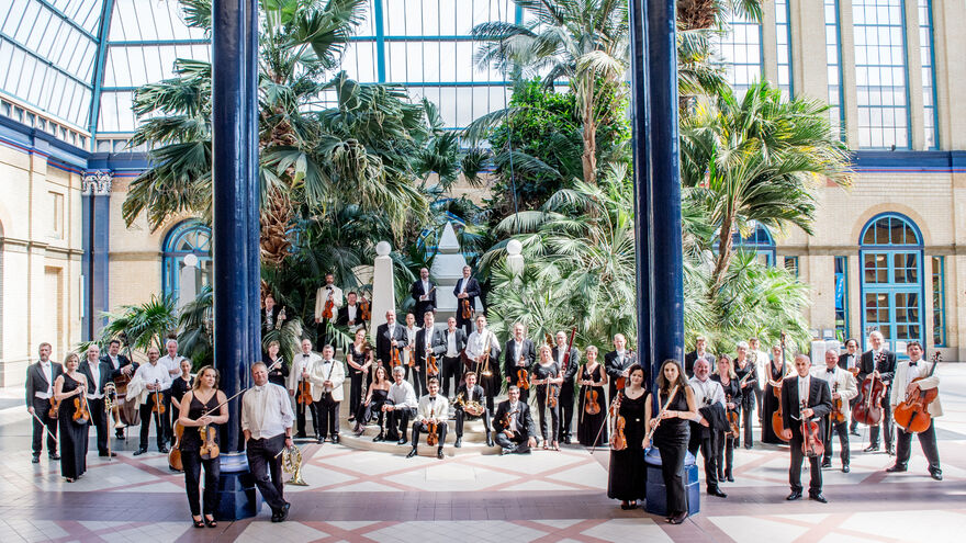 The BBC Concert Orchestra in a large room with a glass ceiling and palm trees