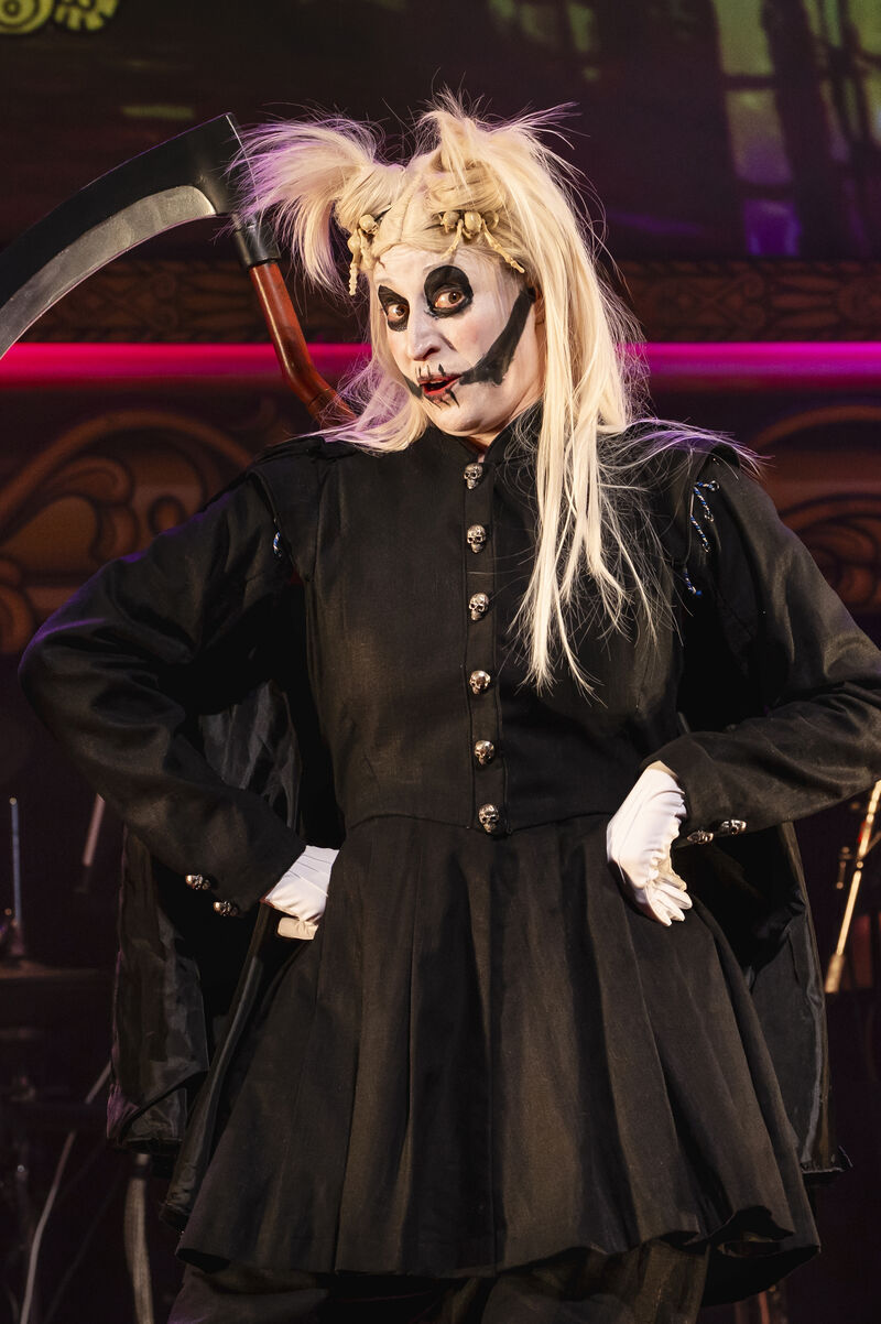 A person dressed as death stands with a pick axe and their hands on their hips