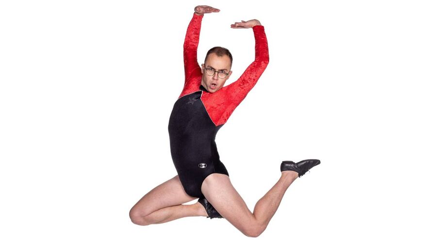Joe Tracini jumping in the air with their arms up. They are wearing a logn sleeve red and black unitard