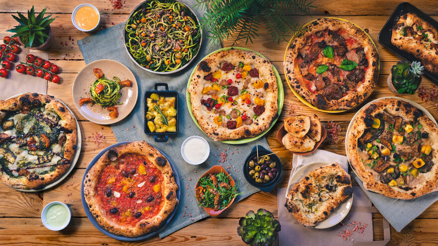 Lots of pizzas and delicious looking sides sit on a wooden table