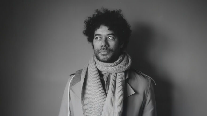 Black and white image of Richard Ayoade wearing a coat and scarf staring at the side