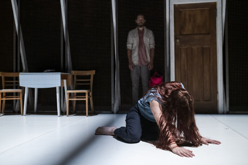 A woman sits collapsed on her hands and knees while her male partner looks on behind her