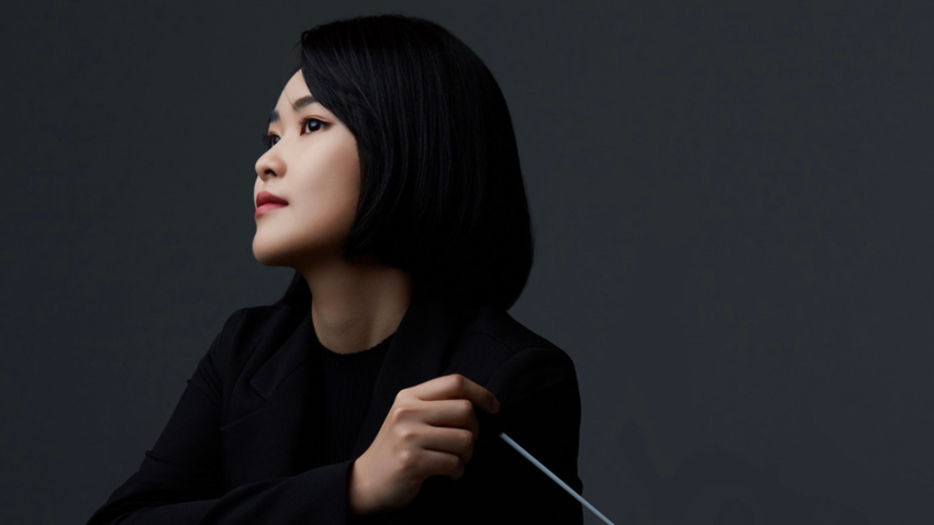Juya Shin holding a conductor's baton staring serenely away from camera