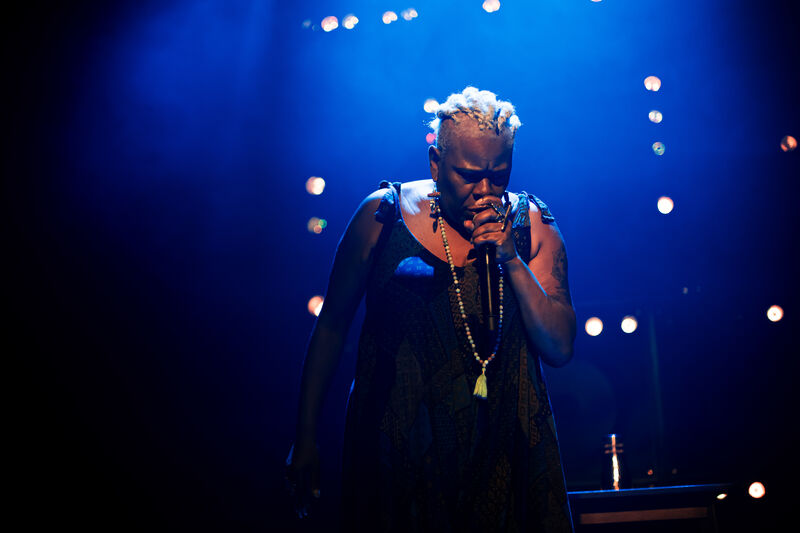 Sutara Gayle lit from behind by blue lights singing into a microphone