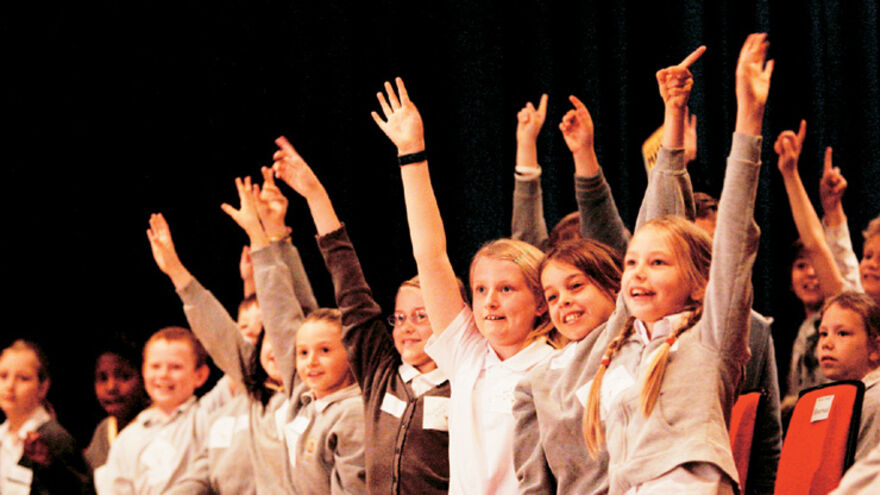 A group of school children excitedly raise their hands 