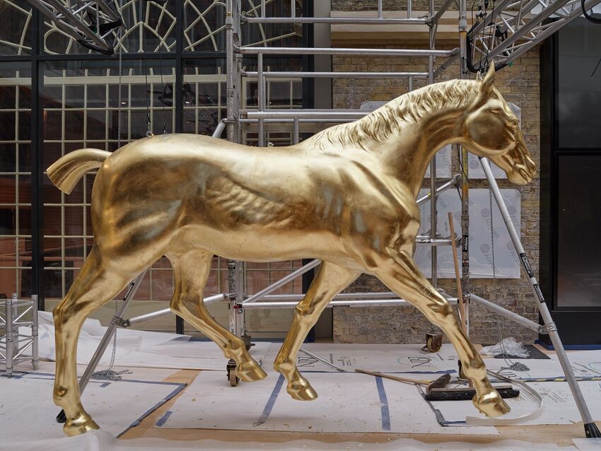 A large model of a horse, fully golden, stands against a backdrop of scaffolding