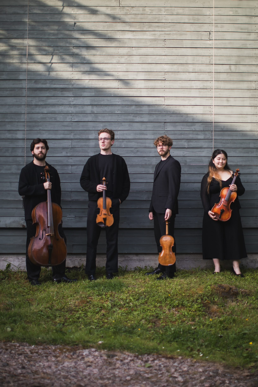Four people in black outfits standing in front of a wooden background. Each person is holding a string instrument.